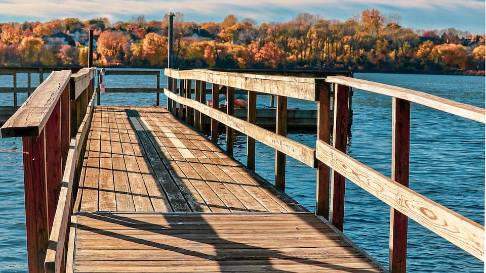 A wooden pier extending into a lake with autumn-colored trees in the background.