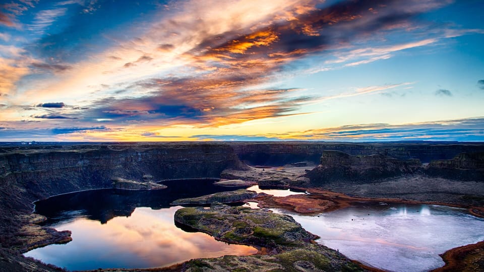 A canyon with reflective water bodies and a sunset sky.