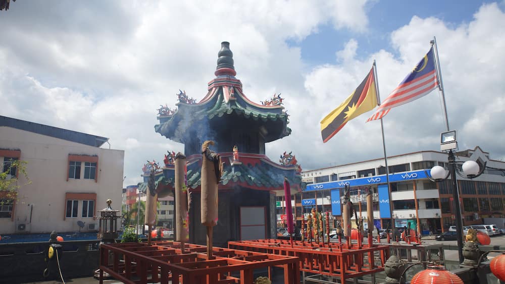 A traditional Chinese pavilion with a dragon statue, surrounded by red lanterns and flags, including the Malaysian flag.