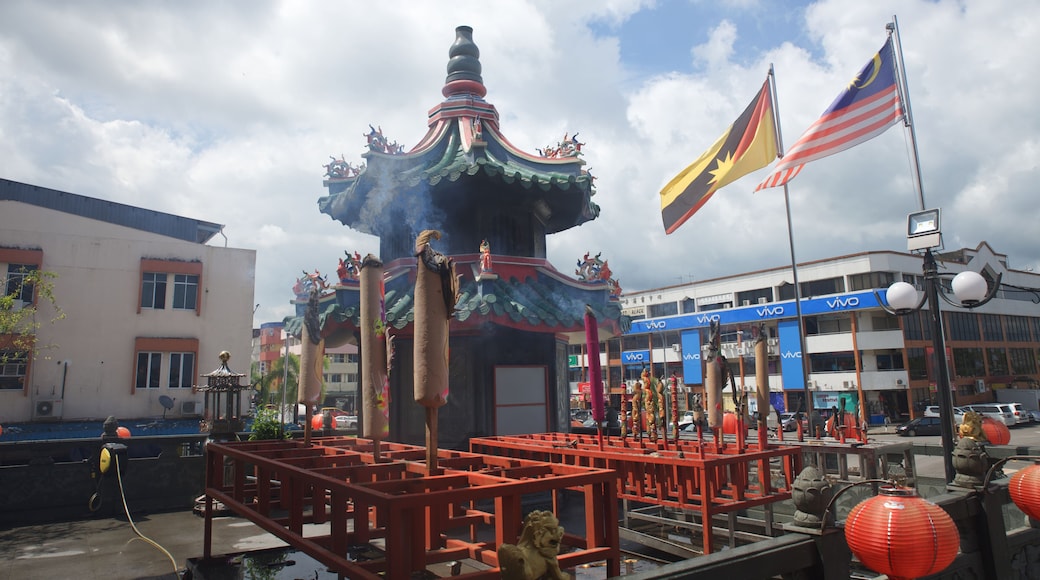 Un pabellón chino tradicional con una estatua de dragón, rodeado de linternas rojas y banderas, incluyendo la bandera de Malasia.