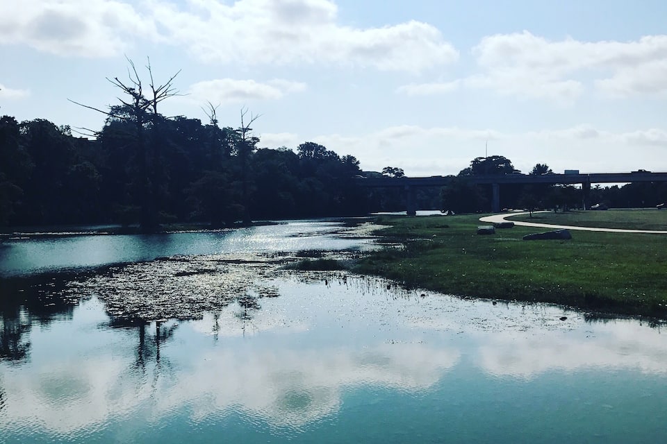 A calm river with reflections of trees and a bridge in the distance.