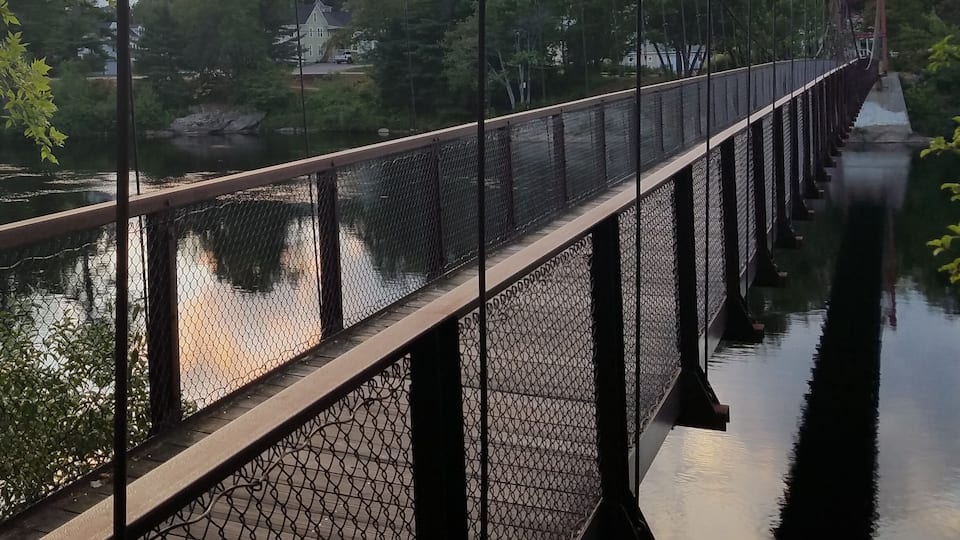 A suspension bridge over a river with a house in the background.