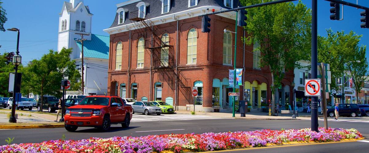 A red car driving on a street with a brick building and a church in the background.