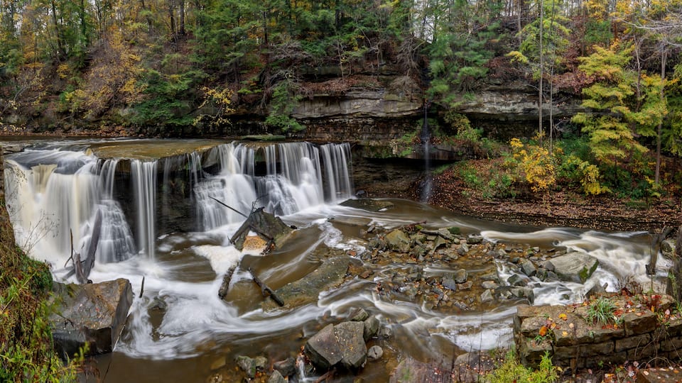 A waterfall cascading over rocks in a forested area with autumn foliage.