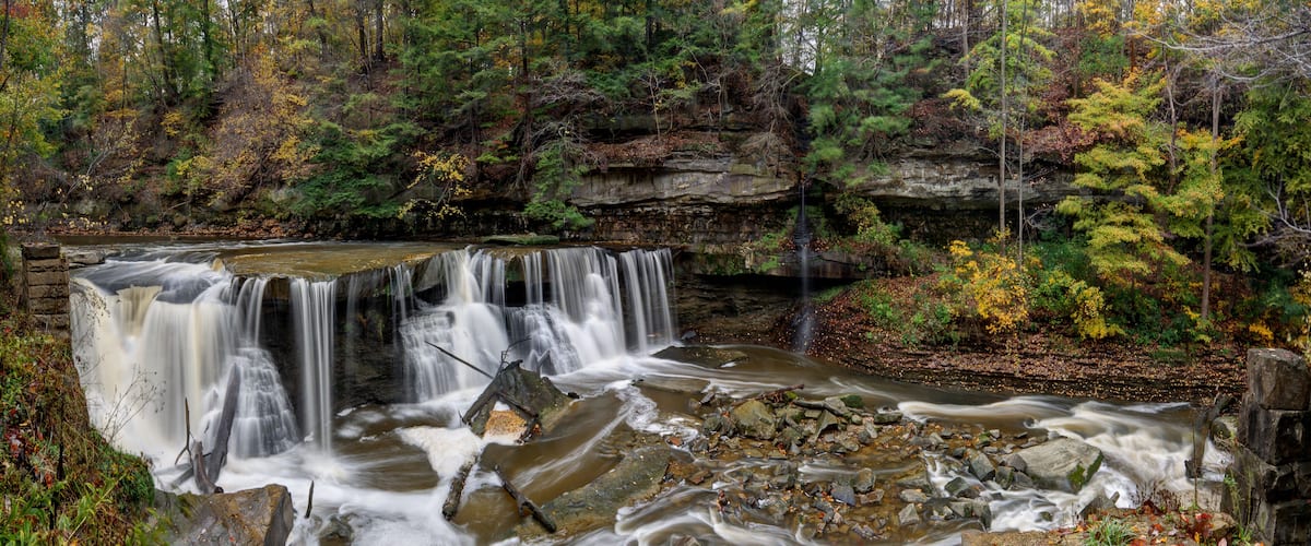 A waterfall cascading over rocks in a forested area with autumn foliage.