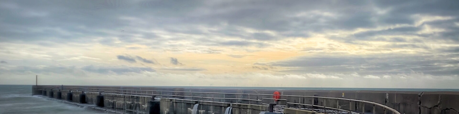 The wall protecting the harbour. Waves were breaking over the wall but still there was someone fishing on the end