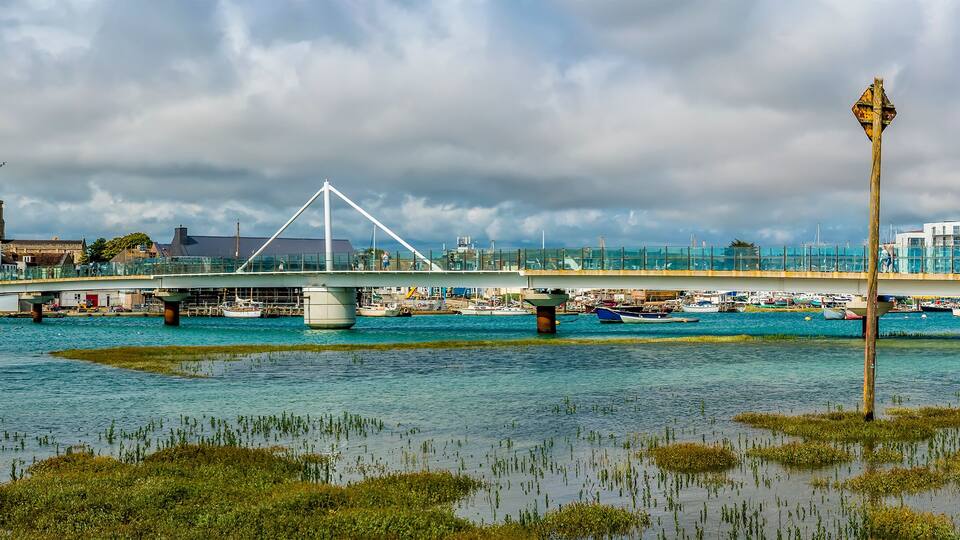 A bridge over water with boats, a tower, and buildings in the background.