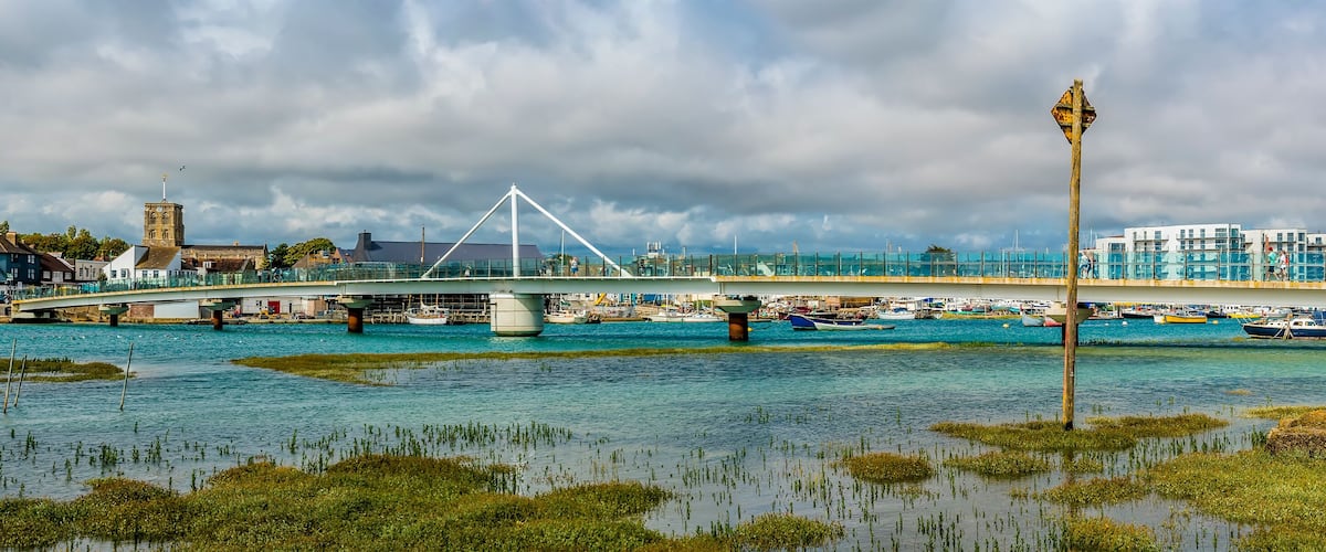 A bridge over water with boats, a tower, and buildings in the background.
