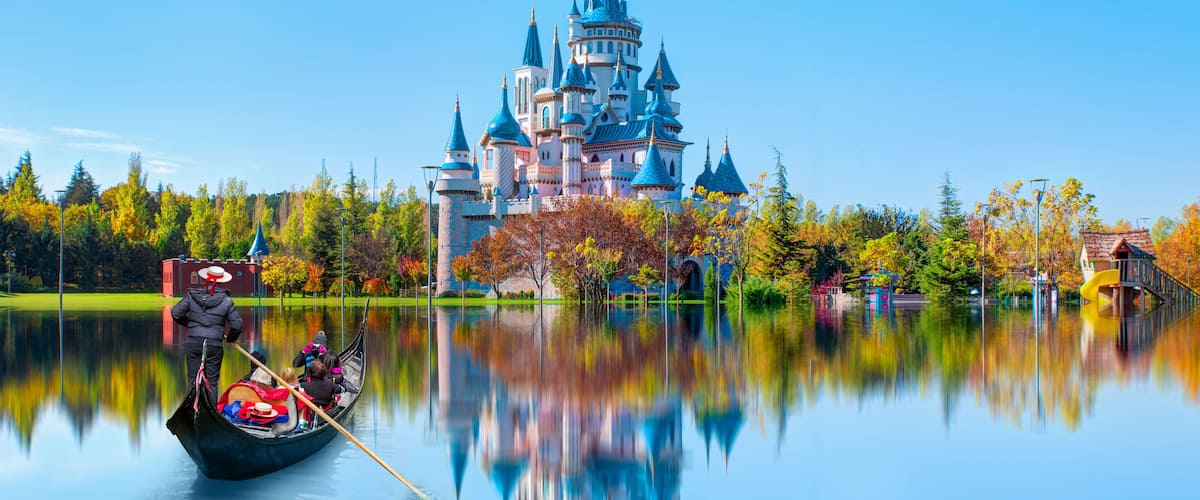 A castle with multiple towers and a gondola on a calm lake.