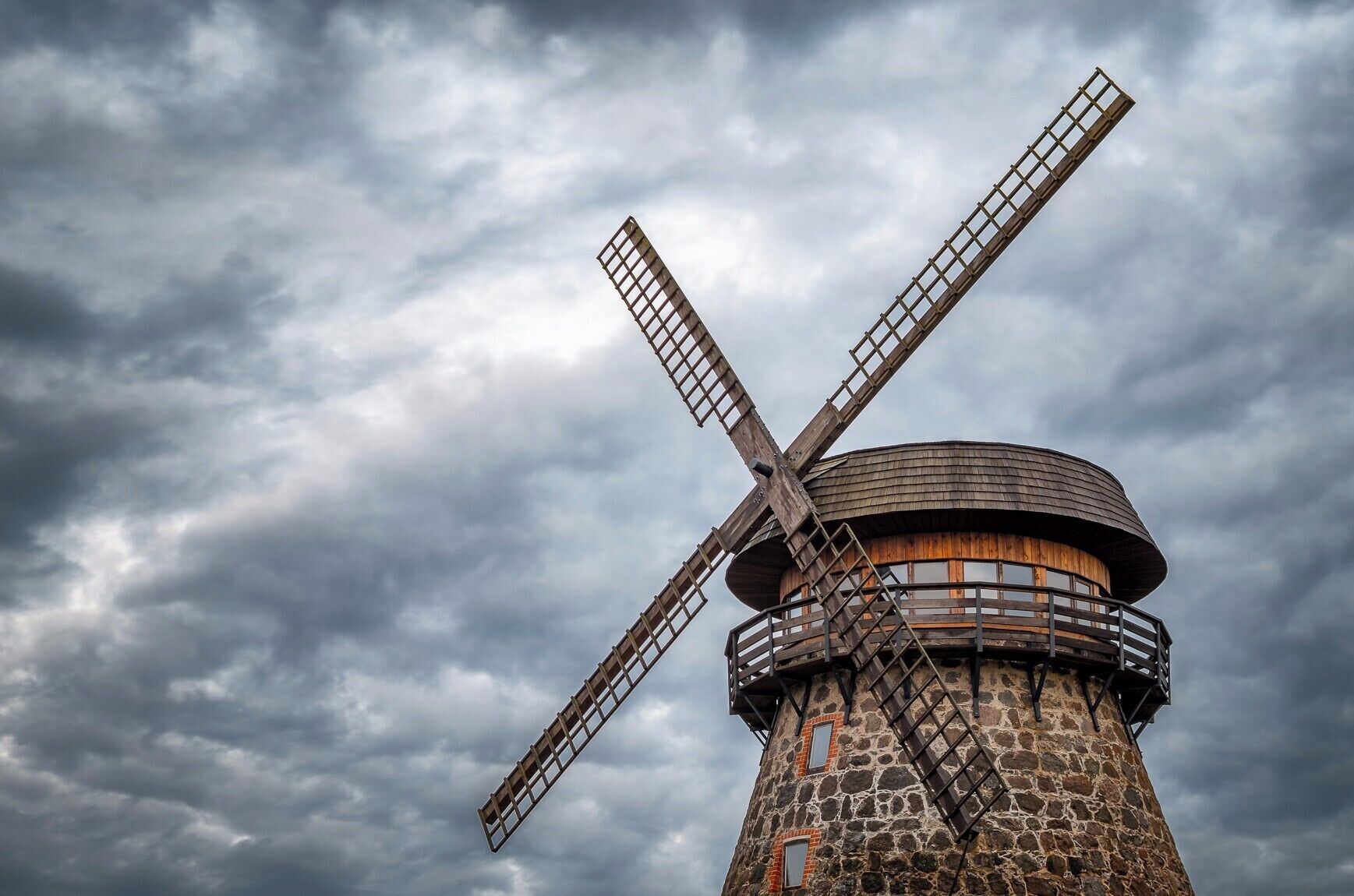 A stone windmill with wooden sails against a cloudy sky.