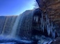 Een waterval die over een rotsklif stort, met ijspegels die aan de rand hangen.