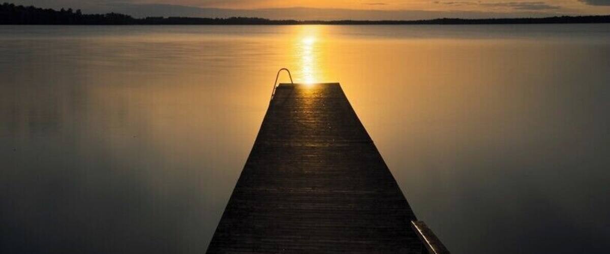 A wooden pier extending into calm water during sunset.