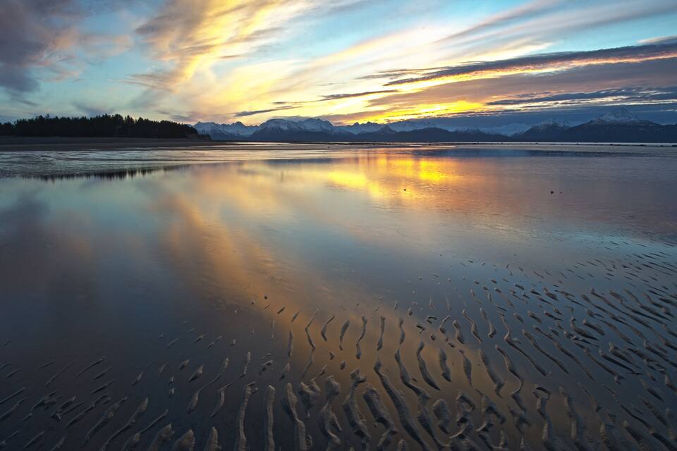A calm lake with ripples, mountains in the background, and a sunset sky.