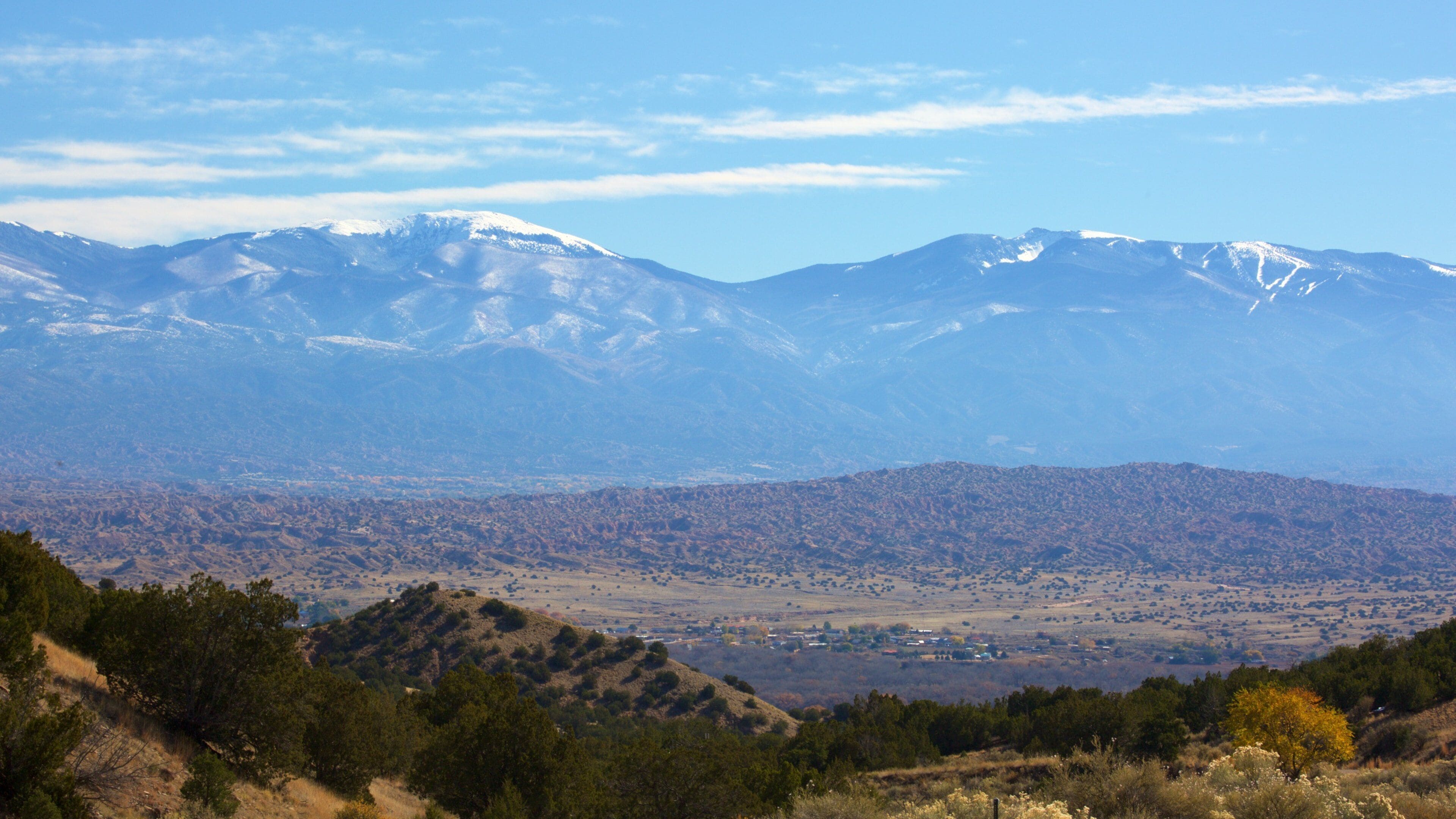 A mountain range with snow-capped peaks, a valley with sparse vegetation, and a clear blue sky.
