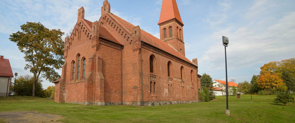 A red brick church with a tall tower and a cross on top.