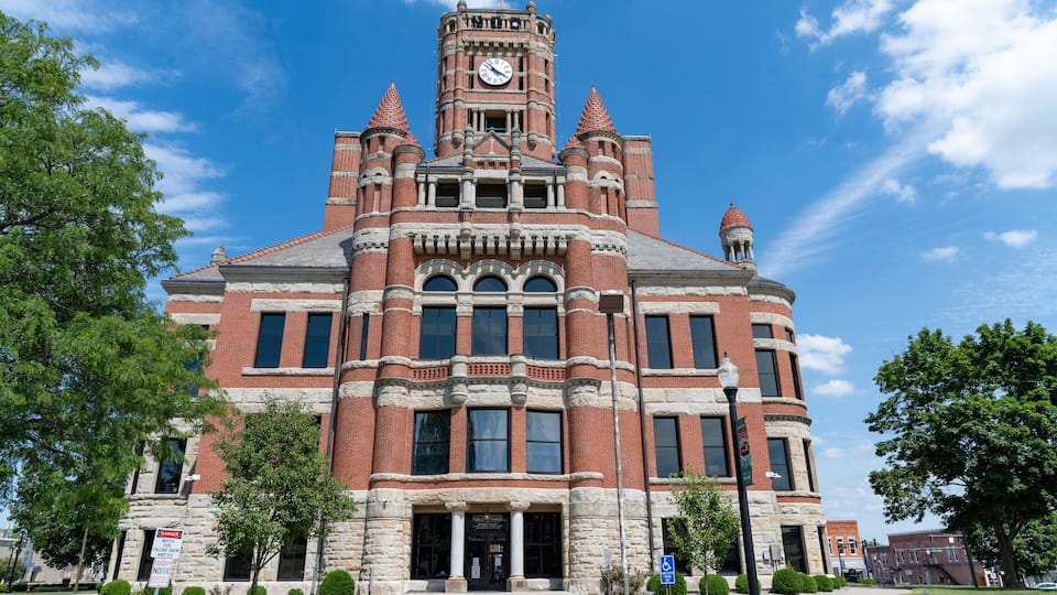 A large, historic brick building with a clock tower, surrounded by trees and a clear blue sky.