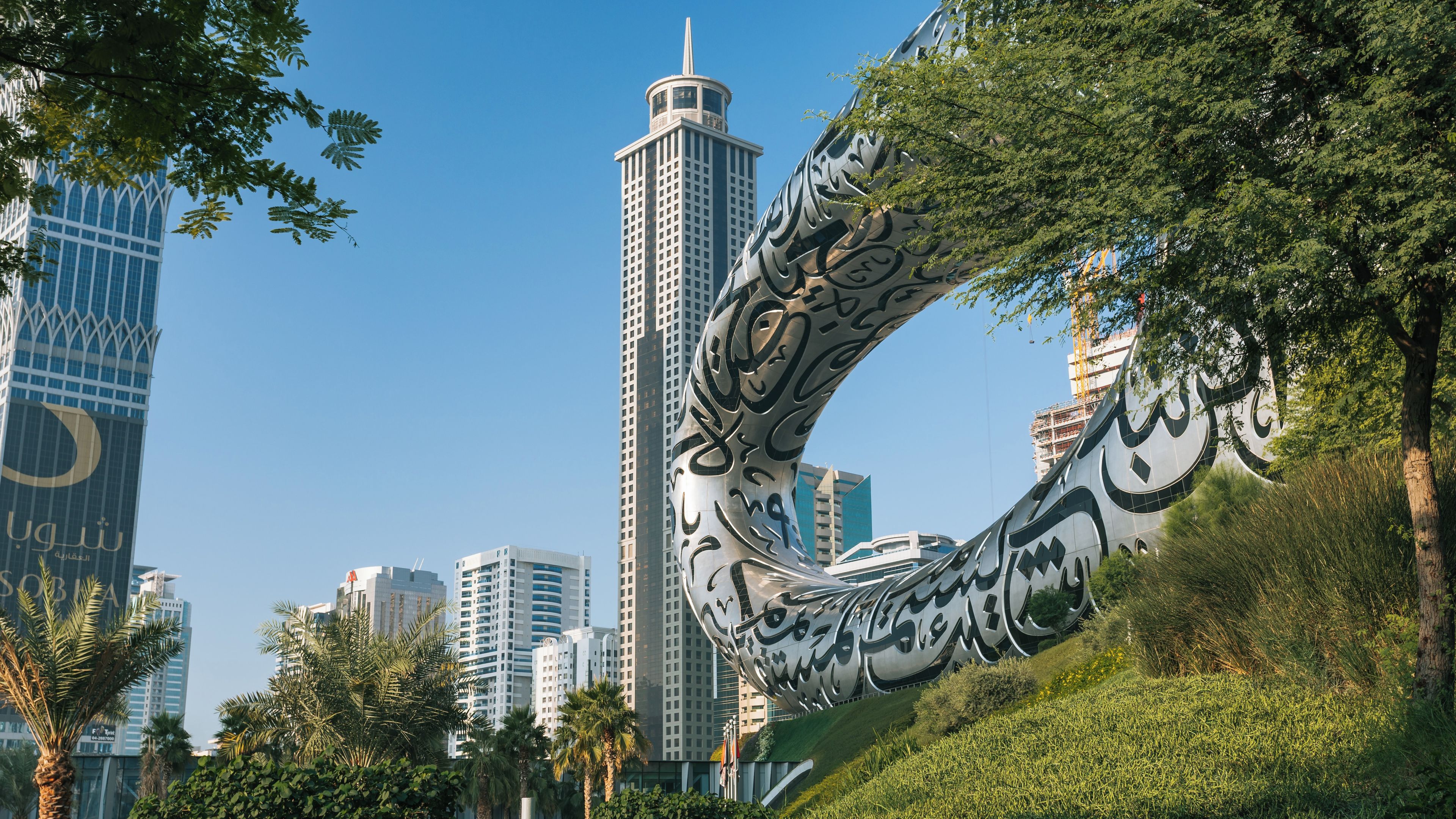 Una escultura moderna con caligrafía árabe, rodeada de palmeras y rascacielos.