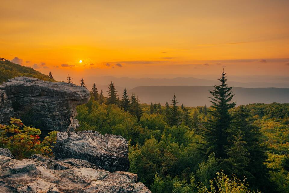Un paysage de montagne avec un coucher de soleil, des affleurements rocheux et une forêt dense.