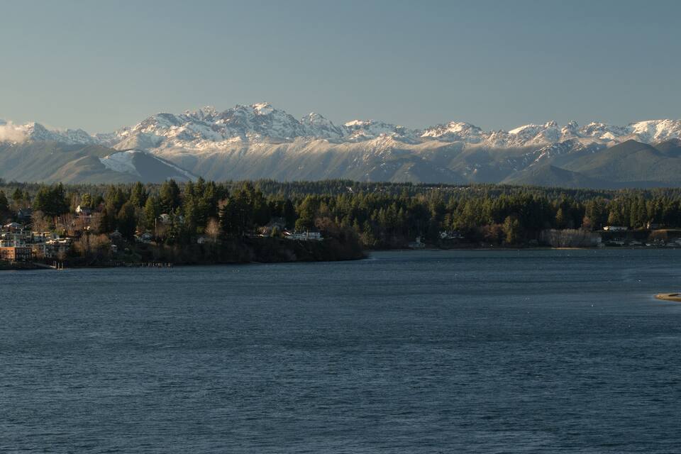 A river with a town on the left and snow-capped mountains in the background.