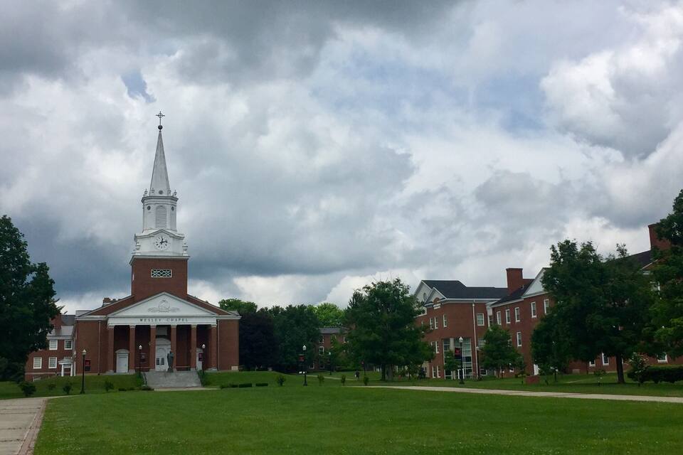 A church with a steeple and a clock tower, surrounded by a grassy lawn and trees.