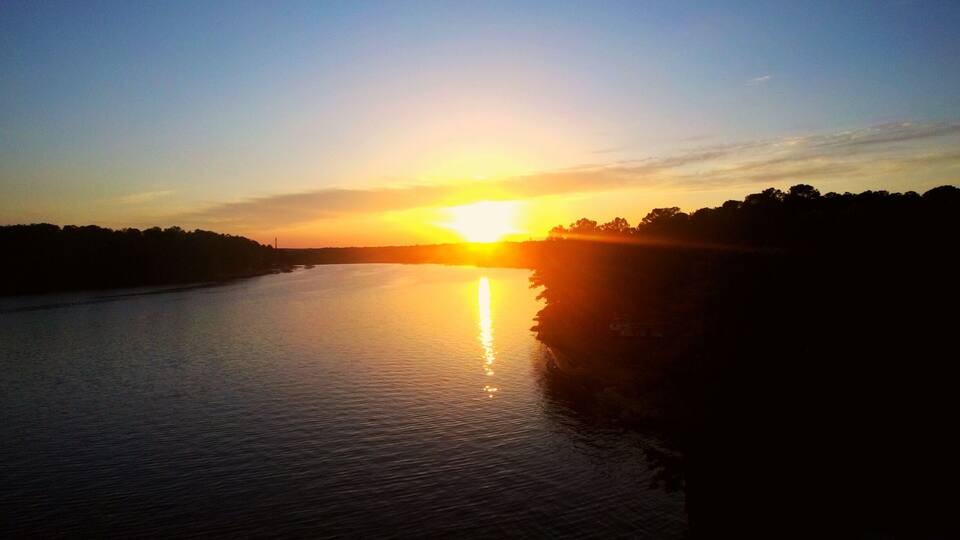 A sunset over a calm river with a silhouette of trees and a distant shoreline.