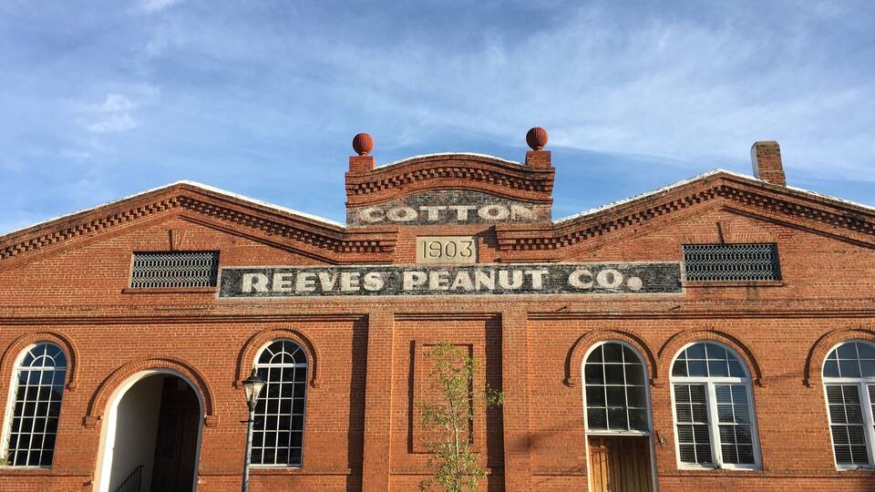 A historic brick building with arched windows and a sign reading "Cotton 1903 Reeves Peanut Co."