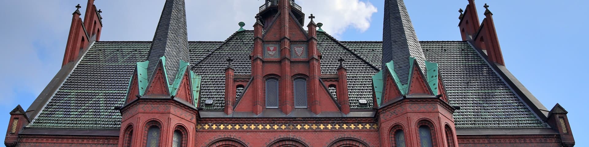 A red brick building with a pointed roof and multiple spires.