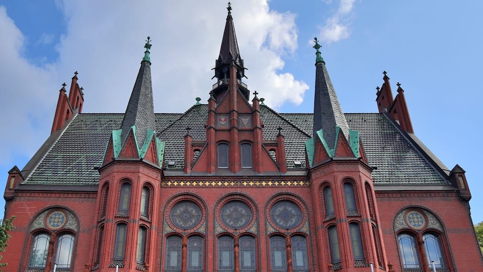 A red brick building with a pointed roof and multiple spires.