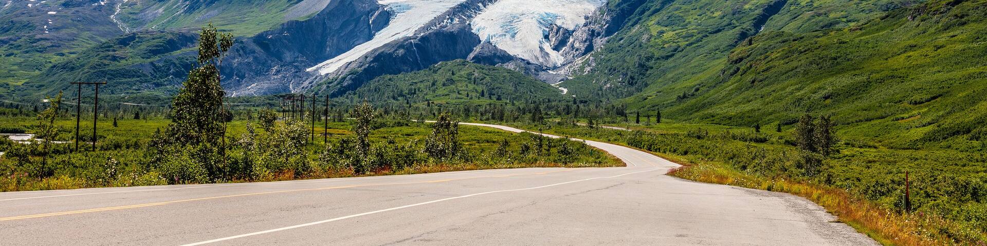 A winding road through a mountainous landscape with snow-capped peaks and a glacier.
