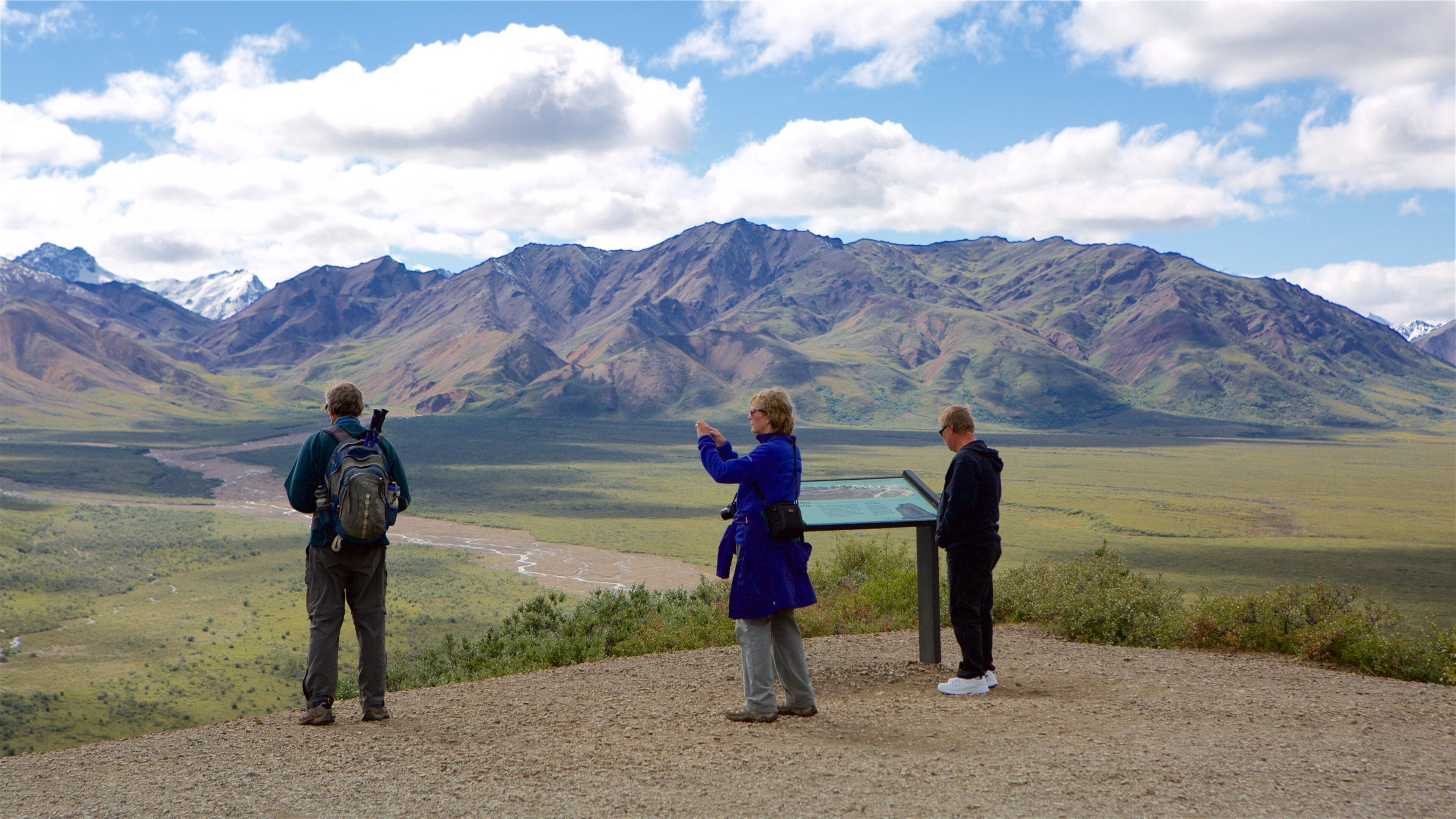 Tres personas observando un paisaje montañoso con un río y una plataforma de observación.