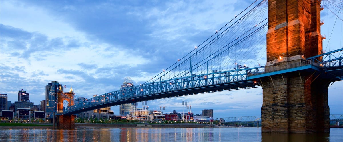 A suspension bridge with a stone tower and a city skyline in the background.