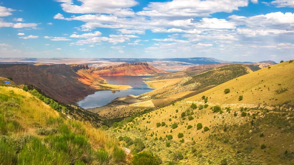 A canyon with a lake, green vegetation, and distant mountains.