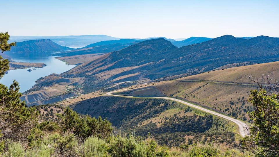 A winding road through a mountainous landscape with a lake in the distance.