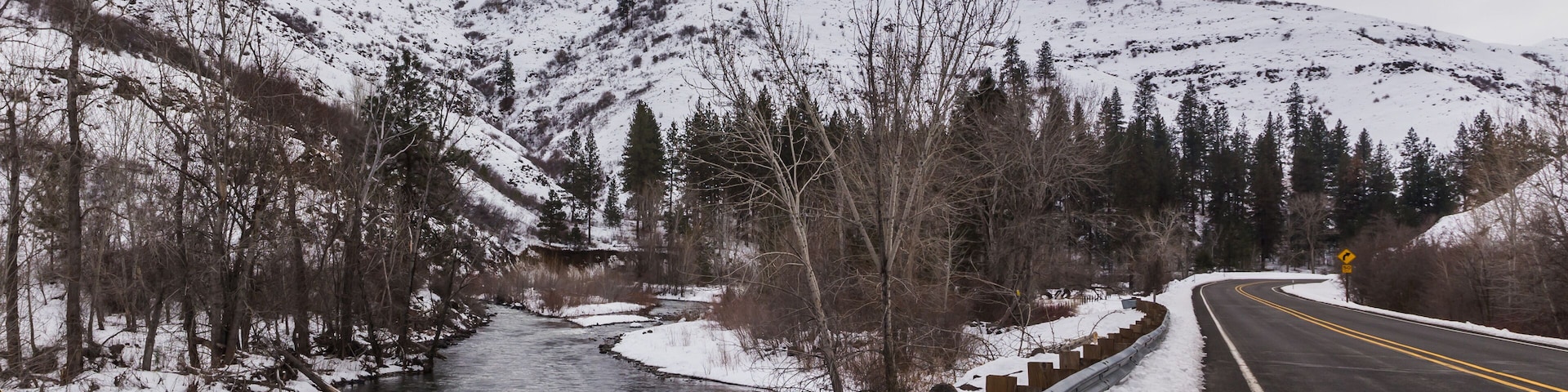 Ein schneebedeckter Fluss mit einer Schutzrail und Bergen im Hintergrund.