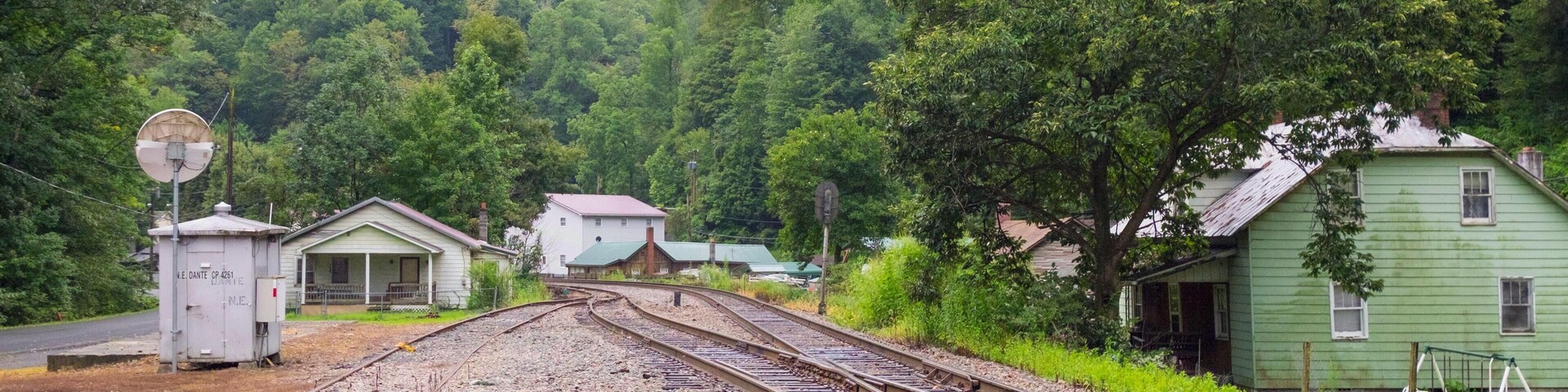 A railway track with a signal box and houses in a forested area.