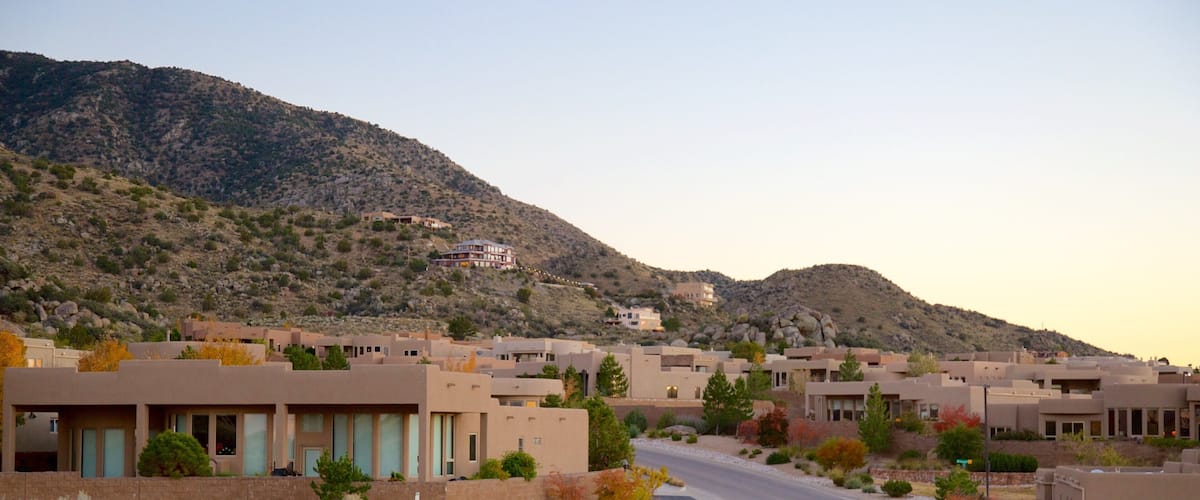 A residential area with modern buildings, a winding road, and a mountainous backdrop.