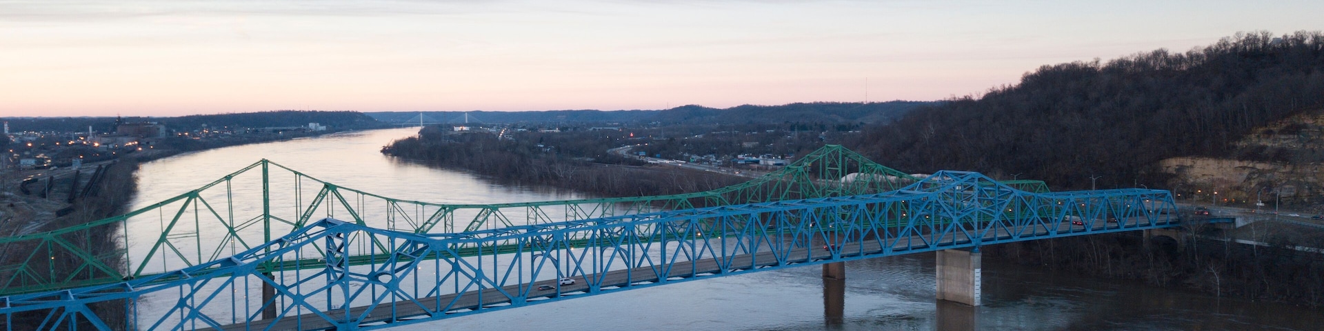 A blue bridge over a river with a cityscape in the background.