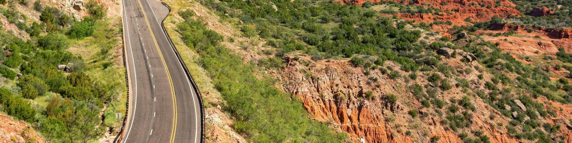 A winding road through a rugged, red-hued landscape with sparse vegetation.