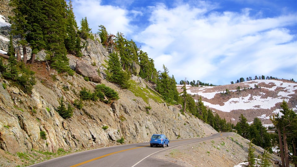 A winding mountain road with a blue car, surrounded by rocky terrain and sparse vegetation.