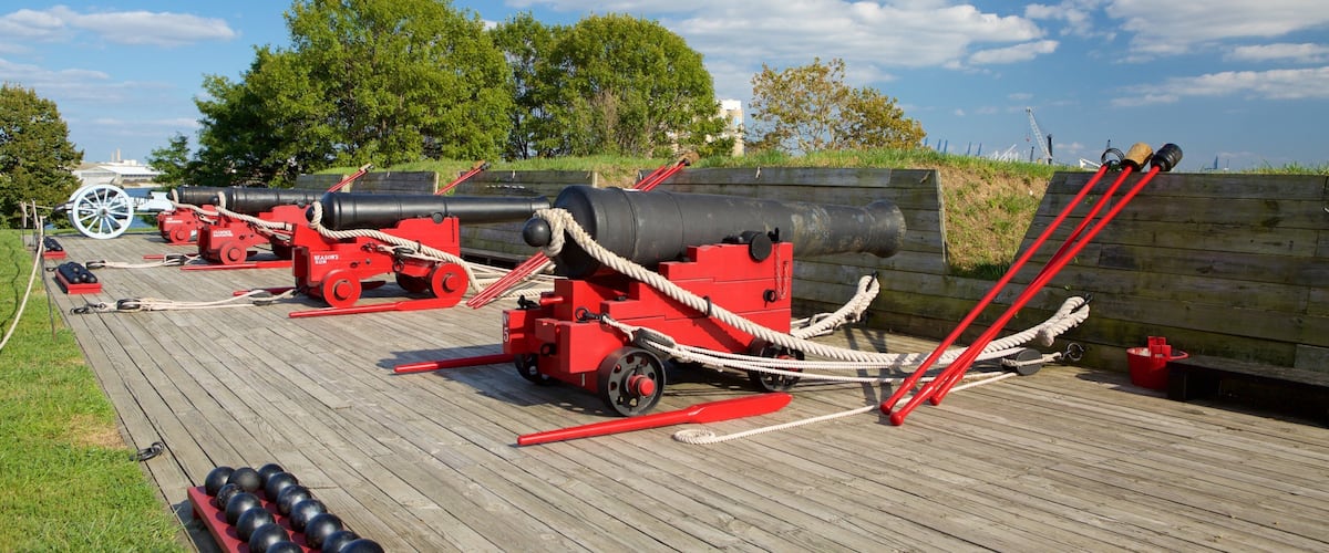 A wooden deck with several red cannons and black cannonballs.