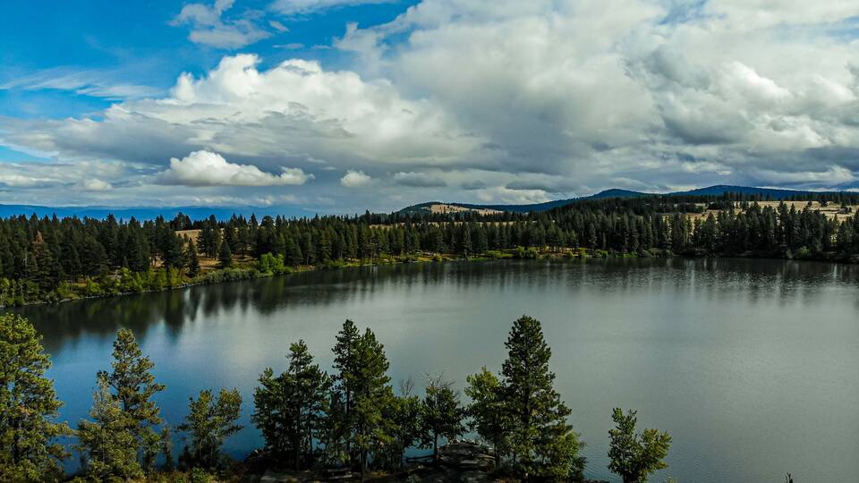 A lake surrounded by trees and mountains under a cloudy sky.