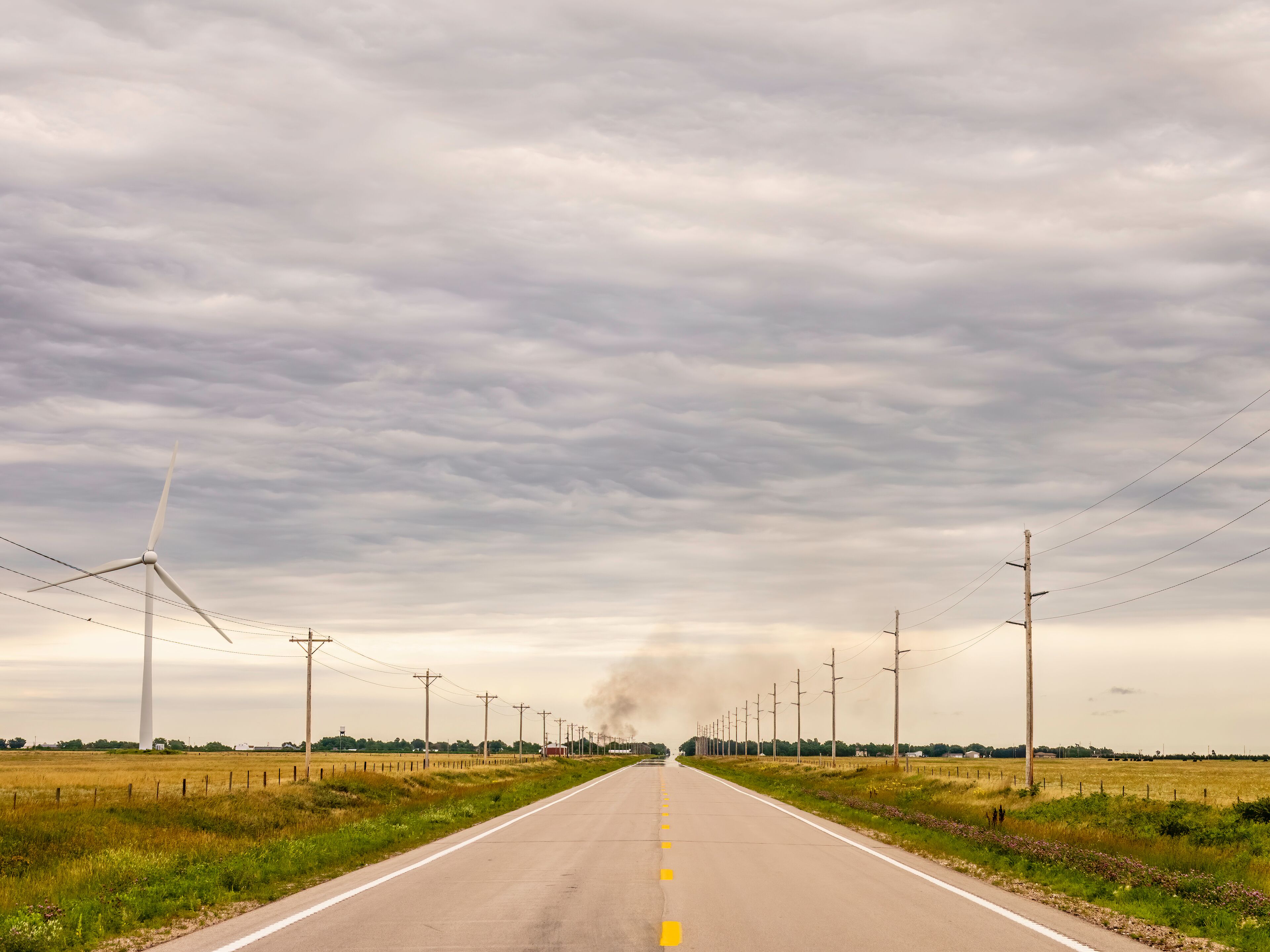 Perspective of Nebraska Highway 12, also known as Outlaw Trail Scenic Byway, with wind turbine (left), smoke rising from a house fire in the town of Springview, and mirage of water across pavement; Sh