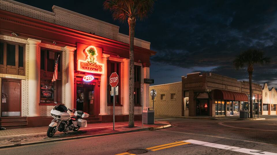 A motorcycle parked in front of a brightly lit building with a neon sign.