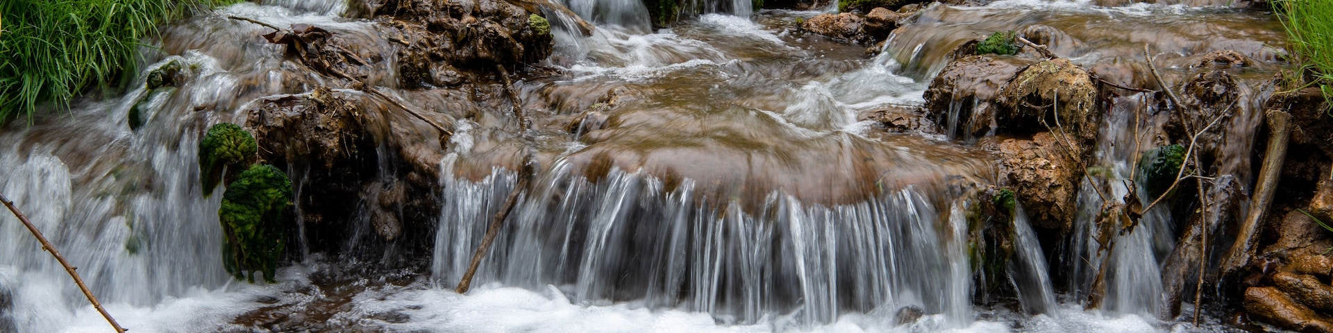 A small waterfall in a lush green area with rocks and moss.