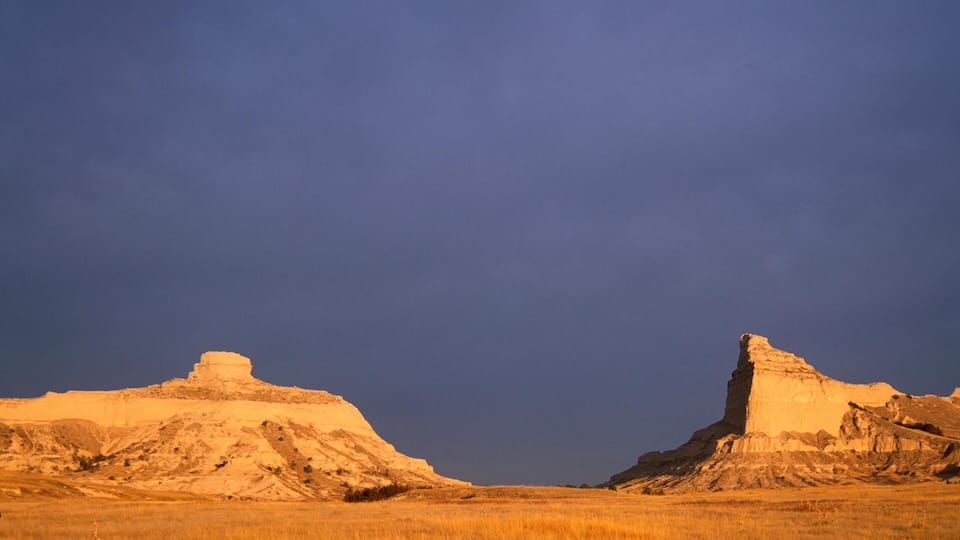 A landscape with two prominent mesas under a clear sky.