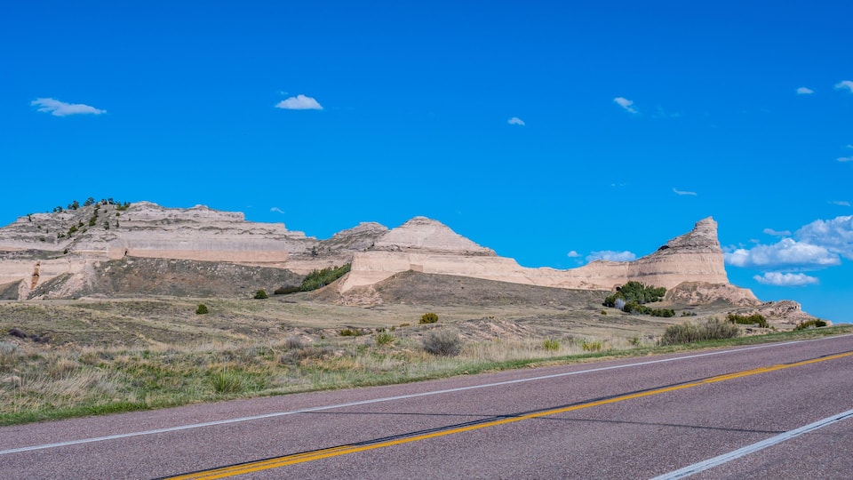 A road with a clear blue sky and rolling hills in the background.