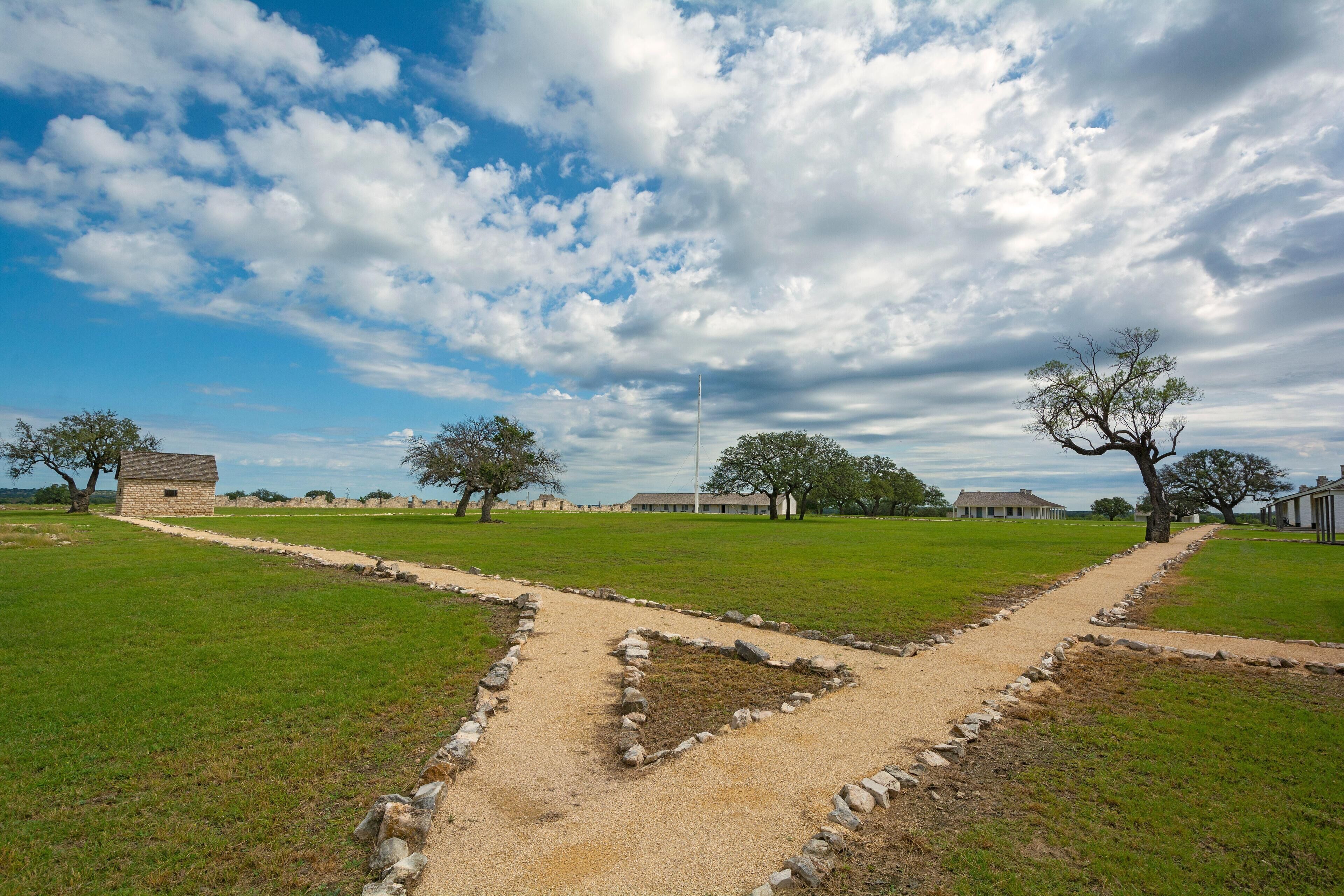 A historical site with a dirt path, stone walls, and scattered trees.