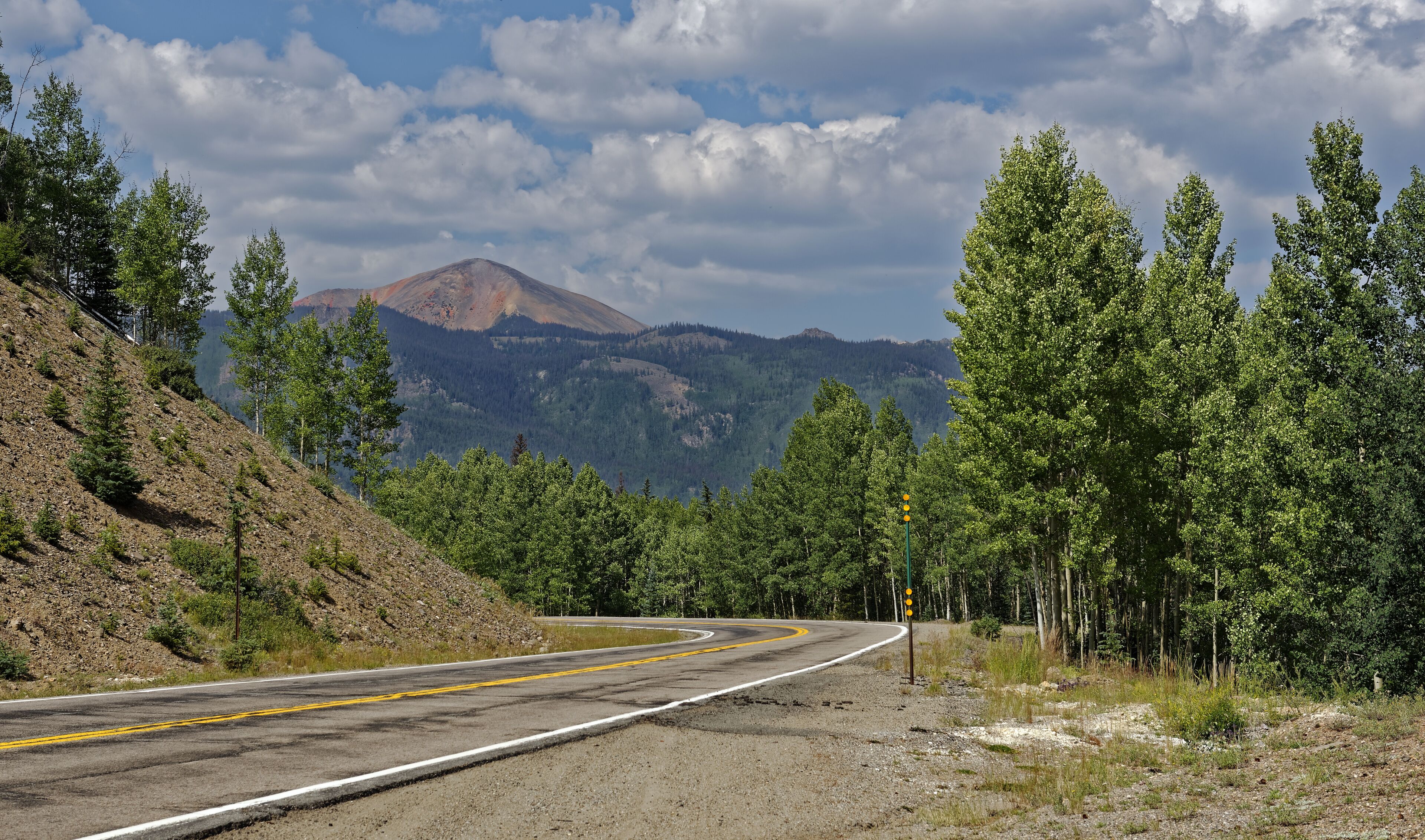 A winding road through a mountainous area with dense forests and a prominent mountain in the background.