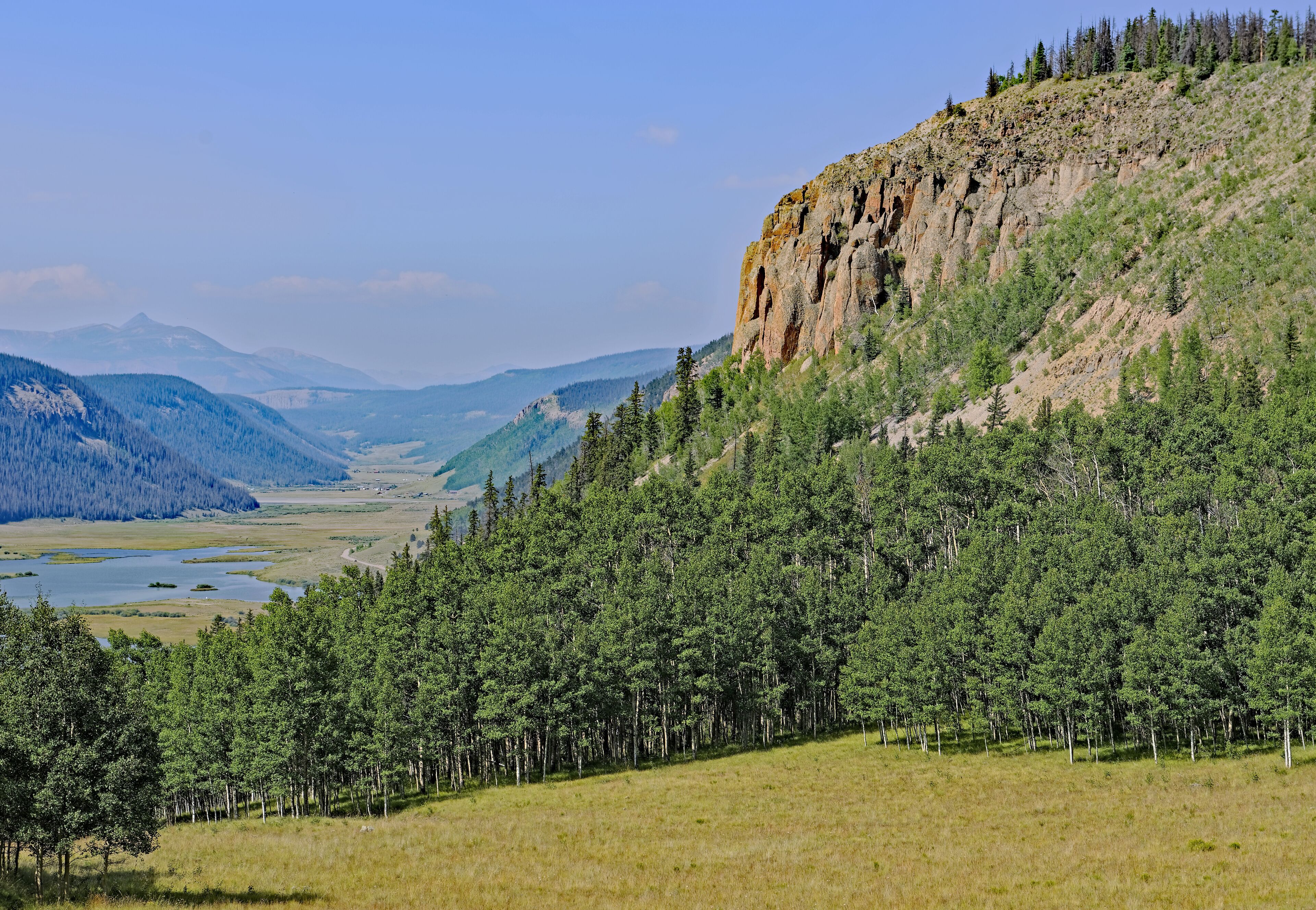 A mountainous landscape with dense forests, a river, and distant mountains.