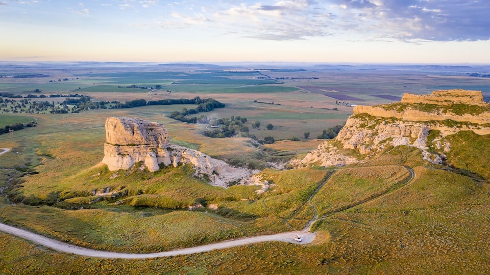 A vast landscape with rolling hills, a prominent rock formation, and a winding road.